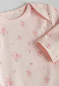 Lyserød langærmet body med lille blomstermønster, lavet af blødt bomuldsmateriale, rund halsudskæring og syede manchetter.