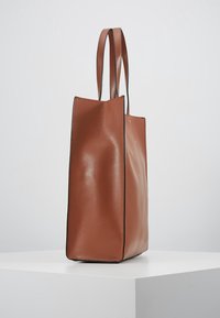 Brązowa skórzana torba typu tote o wyraźnej konstrukcji, teksturowanej powierzchni, dwóch długich uchwytach oraz kontrastowym czarnym obszyciu na krawędziach.