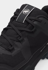 Μαύρο ορειβατικό παπούτσι με υφασμάτινη υφή, μαύρα κορδόνια και λευκό λογότυπο μαμούθ στην ετικέτα της γλώσσας.