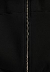 Giacca nera con zip, dotata di una cerniera metallica, caratterizzata da una finitura in tessuto liscio e cuciture pulite, che mette in risalto un design minimalista e moderno.