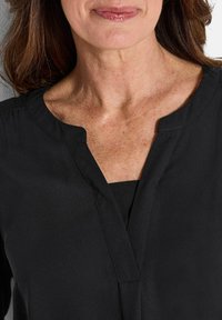 Blusa nera con scollo a V, in tessuto morbido e con una leggera lucentezza. Presenta un design pulito, senza pattern visibili o elementi metallici.