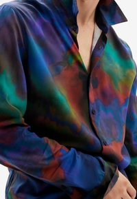 Camicia trasparente a bottoni multicolore che presenta una combinazione di tonalità blu, verde e rossa, con una consistenza morbida e un design del colletto rilassato.