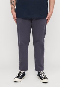 Slim-fit, dark gray pants made of cotton twill, featuring a smooth texture and classic five-pocket design, paired with black high-top sneakers.