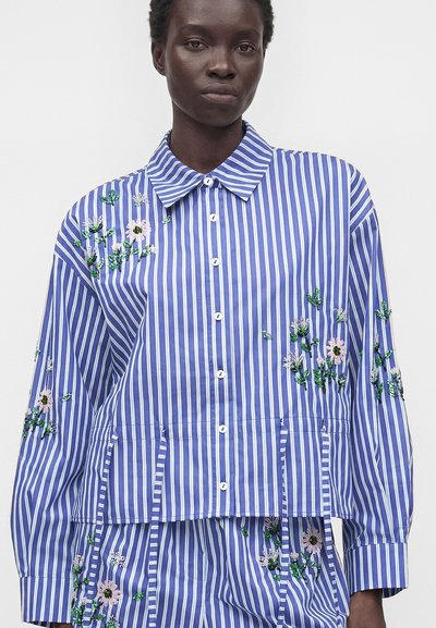 Person wearing blue and white vertical striped shirt and pants with embroidered green and pink floral patterns on sleeves and torso.