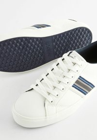 Weiße Sneakers mit blauen und grauen gestreiften Akzenten, strukturiertem Gummi-Außensohle und weißen Schnürsenkeln. Glattes synthetisches Obermaterial mit Stickdetails.
