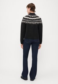 Zwarte gebreide trui met wit patroonontwerp op de schouders, gecombineerd met donkerblauwe uitlopende jeans. Soepele textuur en casual pasvorm.