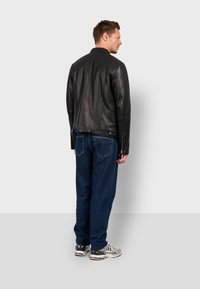 Chaqueta de cuero negra con un diseño ajustado, puños con cremallera y una textura suave, combinada con jeans de mezclilla azul y zapatillas.