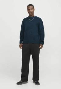 Marineblauer Strickpullover mit strukturiertem Finish, lässigem Schnitt und gerippten Bündchen, kombiniert mit schwarzen weit geschnittenen Hosen und schwarzen Sneakers.