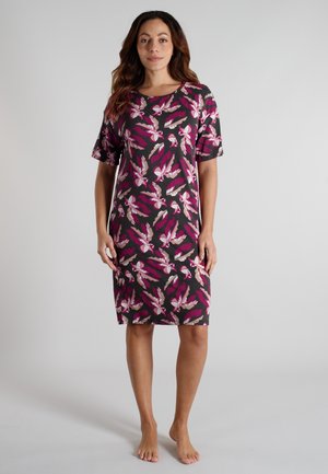 Woman standing barefoot wearing a black knee-length dress with short sleeves and pink, white, and beige leaf patterns.