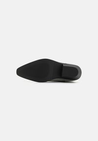 Suela de zapato negra con punta afilada y superficie texturizada. El diseño presenta un acabado suave y pulido con surcos sutiles para tracción.