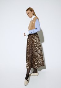 Chaleco de punto beige sobre camisa azul clara, combinado con una falda de estampado de leopardo marrón. La modelo lleva zapatos blancos y medias negras.