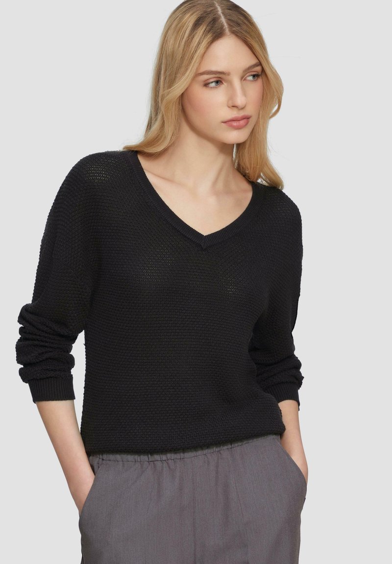 Maglione nero a maglia con scollatura a V, vestibilità ampia e maniche lunghe. Dettaglio di tessuto testurizzato, abbinato a pantaloni grigi chiari con vita elastica.