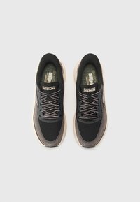 Chaussures de sport noires avec tige en mesh, semelle claire et accents réfléchissants argentés. Comprend des lacets, un col rembourré et un logo sur la languette.