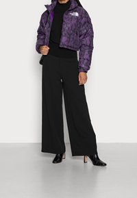 Fioletowa kurtka puchowa w panterkę, czarny lekki top z długim rękawem, czarne spodnie szerokie w nogawkach oraz czarne botki na obcasie.