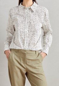 Wit langemouwen overhemd met een zwart gespetterd patroon. Voorzien van een kraag en een comfortabele pasvorm. Gecombineerd met lichtbeige op maat gemaakte broeken.
