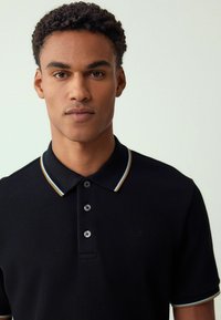 Schwarzes Polohemd aus strukturiertem Stoff, mit dreiknöpfiger Knopfleiste und kontrastierendem Kragen in Hellblau und goldenen Akzenten.