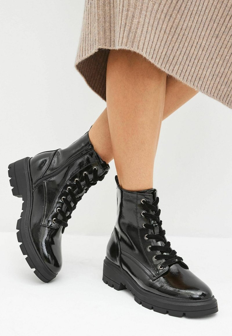 Bottines à lacets en cuir verni noir avec une semelle épaisse, dotées d'œillets métalliques et d'une texture lisse. Les bottines présentent un design à bout arrondi.