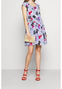 Uppblåst klänning i ljus lila med abstrakta hjärtmönster i rött, svart och grått. Matchas med röda klackar och en guldfärgad clutch.