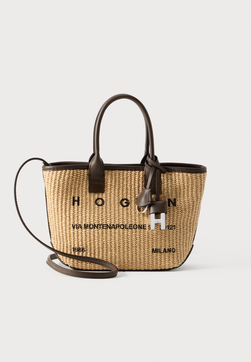 Bolso de paja tejido con detalles en cuero marrón, que incluye una correa para el hombro desmontable, letras del logo y una etiqueta decorativa de cuero.