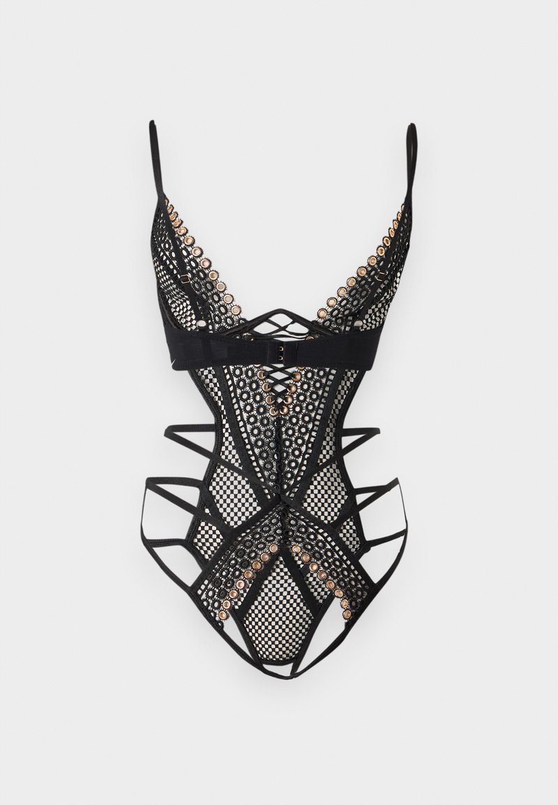 Body en dentelle noire avec découpes complexes, panneaux en maille, bretelles réglables et accents œillets dorés sur fond blanc.