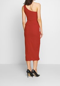 Röd, åtsittande, enaxlad midiklänning med en jämn textur. Bärs med svarta högklackade skor. Enkel design med en sidoklyvning i fållen.