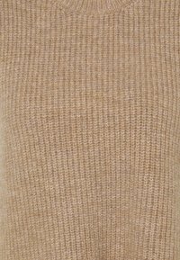 Pull en tricot beige avec une texture côtelée. Encolure ronde et tissu doux et confortable. Design simple sans motifs ni accents supplémentaires.