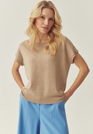 Beige strikket top med korte ærmer, rund halsudskæring, afslappet pasform og ribbet kant, kombineret med lyseblå bukser med vide ben.