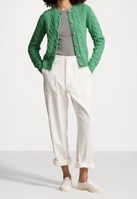 Grön kabelstickad cardigan med rund halsringning, knäppning fram och en grå tajt skjorta under. Kombinerad med vita lösa byxor och vita sneakers.