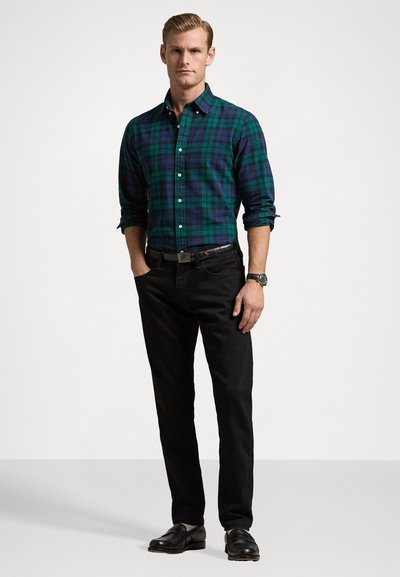 Heren groen en zwart geruite button-up shirt, zwarte rechte jeans en zwarte schoenen. Het shirt heeft lange mouwen en een kraag. Classic fit.