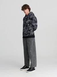 Bluza z kapturem w czarnym kolorze z szarymi wzorami w stylu graffiti; w zestawie z luźnymi szarymi jeansami i czarnymi trampkami. Gładka tekstura.