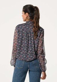 Vloeiende, doorschijnende blouse met een donker marineblauwe achtergrond, bloemen-paisleypatroon in rood en groen, lange mouwen en een geplooid ontwerp aan de achterkant.