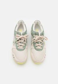 Ett par beiga och gröna mesh-sneakers med snören som är knutna, sett ovanifrån mot en ren vit bakgrund.