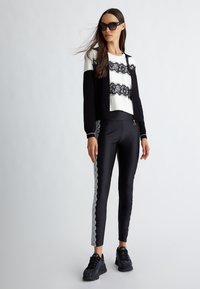 Schwarz-weiße Outfits mit einem Oberteil mit Spitzenakzenten und eleganten schwarzen Leggings mit Spitzen-Seitenpanelen, kombiniert mit schwarzen Sneakers und Sonnenbrille.