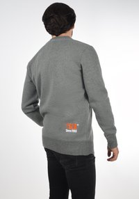 Gray sweatshirt made of soft material, featuring a round neckline and ribbed hem, with an orange logo and text at the back bottom corner.