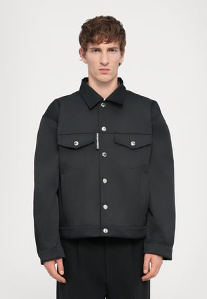 Schwarze Jacke mit strukturiertem Design, ausgestattet mit einem Kragen, zwei Fronttaschen, metallischen Knöpfen und kontrastierenden Stickdetails.