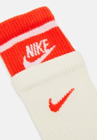 Cotton blend socks in orange and white with ribbed texture. Features "Nike" logo in white on the orange cuff and a small red swoosh on cream body.