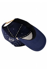 Gorra de béisbol azul marino con patrón blanco de anclas, tela suave, visera curva, forro negro y correa ajustable en la parte posterior. El interior tiene detalles del logo.