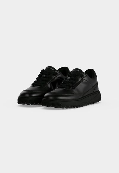 Ζευγάρι μαύρα δερμάτινα sneakers χαμηλού τύπου με παχιές υφασμάτινες σόλες και μαύρα κορδόνια σε απλό ανοιχτό φόντο.