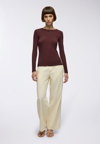 Czarna bluzka z długim rękawem zestawiona z szerokimi jasnymi spodniami, miękkie tekstury, gładki materiał i jasne sandały. Minimalistyczny design.