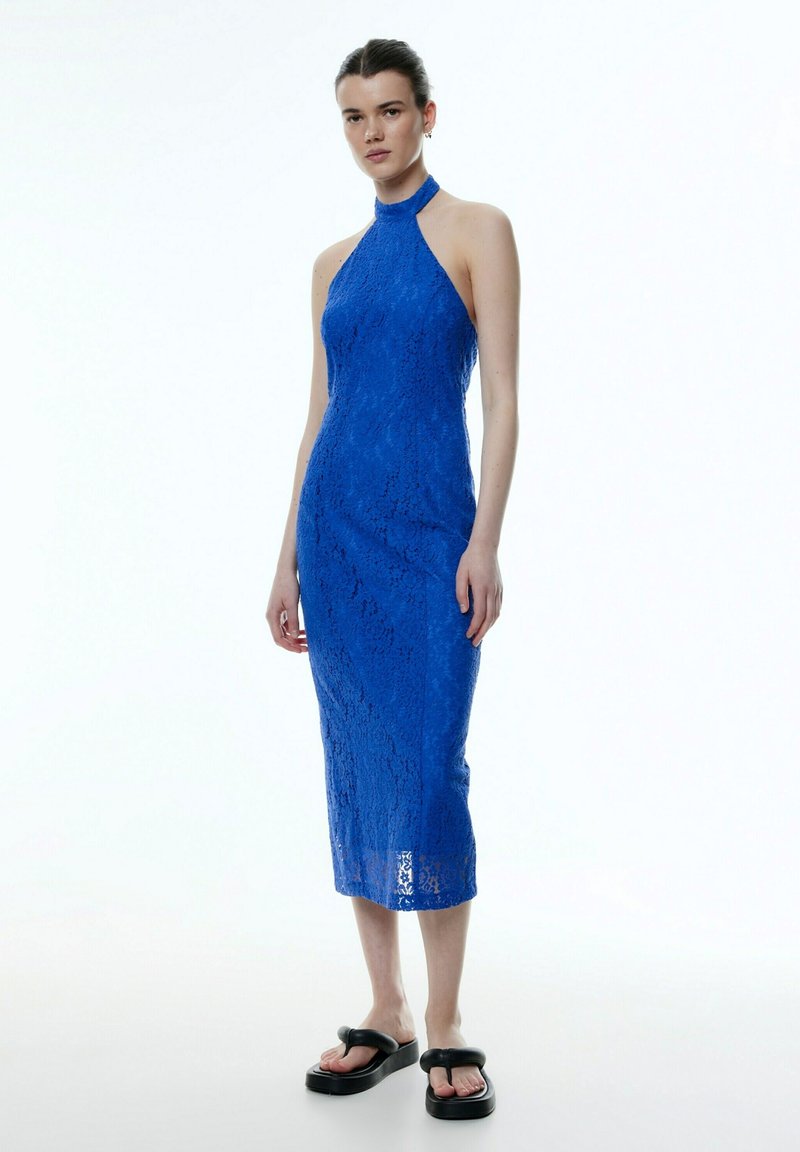 Blaue Spitzen-Halskappendresse mit passender Silhouette, knielang und mit komplexer Spitzenstruktur. Kombiniert mit schwarzen Plateausandalen.