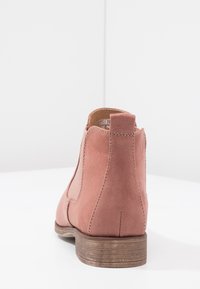 Bota de ante rosa hasta el tobillo con punta redonda, paneles laterales elásticos y un tacón de madera apilada marrón, con costuras limpias y un acabado suave.