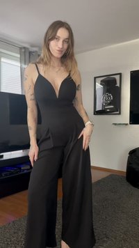 Macacão preto com um decote em V profundo, alças finas e um design de perna larga. O tecido tem uma textura suave e apresenta detalhes plissados.