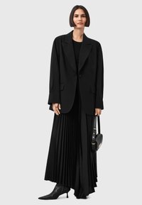 Blazer oversize nero, gonna maxi plissettata nera, top aderente nero, stivaletti neri con punta a punta e una piccola borsa nera.
