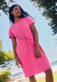 Robe rose à manches courtes avec un détail torsadé à l'avant et une coupe décontractée. Confectionnée dans un tissu doux, elle présente une longueur au genou et une texture lisse.