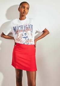 Biała koszulka z grafiką "Michigan Great Lakes" w niebieskim i pomarańczowym kolorze, zestawiona z czerwoną mini spódnicą. Gładki materiał o dopasowanym kroju.