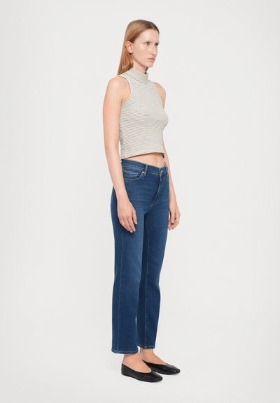 Top corto a righe in grigio e bianco, abbinato a jeans a gamba dritta blu scuro. Indossato con ballerine nere, hardware minimal, texture liscia.