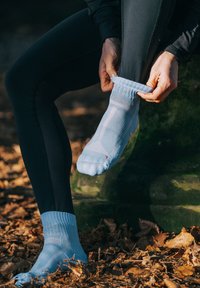 Calze sportive azzurro chiaro con polsini a coste, modelli testurizzati e una vestibilità aderente, indossate su una gamba con leggings neri contro uno sfondo naturale.