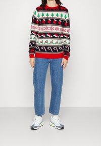 Sweter dzianinowy z festywnymi wzorami w kolorach czerwonym, zielonym i czarnym, przedstawiający choinki, skarpety i lizaki. Ściągacze przy mankietach i u dołu.