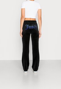 Svarta velour sweatpants med rhinestone "Juicy"-logotyp på baksidan, kombinerat med en vit cropped t-shirt och sneakers. Slen yta, avslappnad passform.