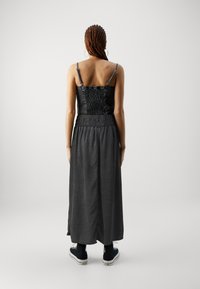 Robe maxi avec un corsage noir ajusté, texture smockée et une jupe grise fluide. Elle possède des bretelles ajustables et est portée avec des baskets noires.